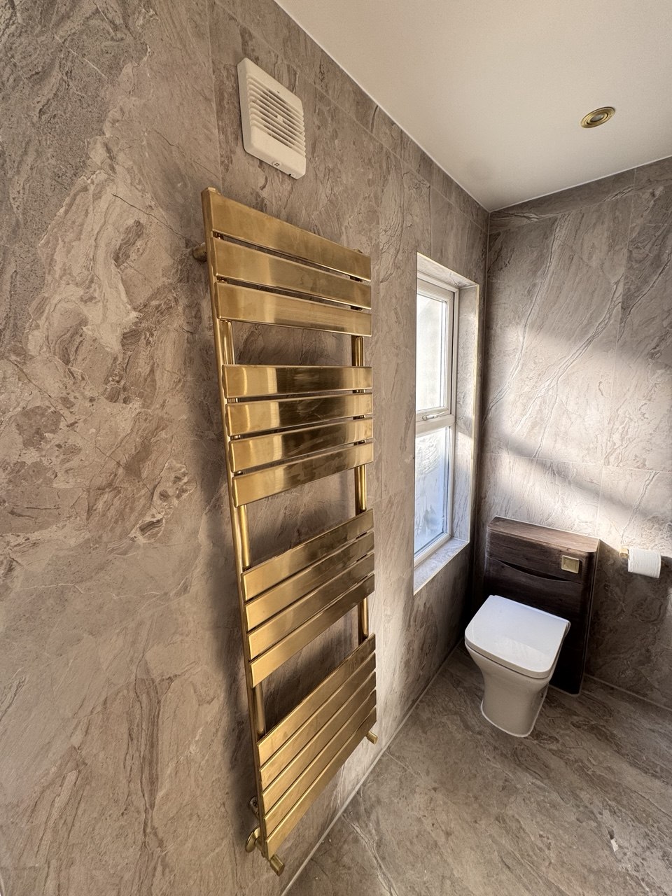 Brushed gold heated towel rail with marble wall tiles